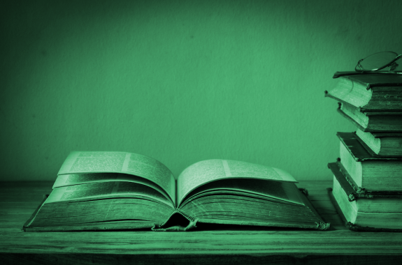 old open book on table next to stack of books with green color