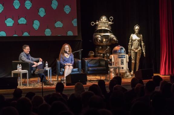 justine cassell is interviewed on stage in pittsburgh. in the background are a bunch of robots