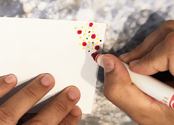 a person coloring the corner of a white square paper with a marker