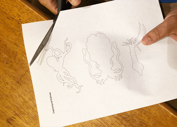 a pair of scissors cutting a piece of paper with cephalopod outlines on it