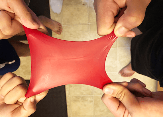 two pairs of hands pulling four corners of a red balloon