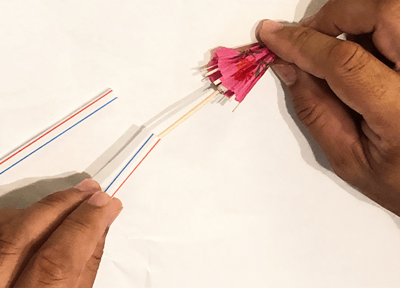 hands placing a cocktail umbrella into the end of a straw