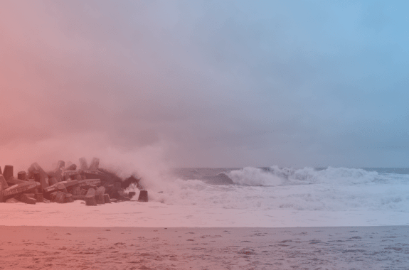 a blue and red tinted photo of a beach with waves crashing to show under a gray sky
