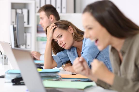 Worried worker beside a successful one who is excited reading good news on line at office