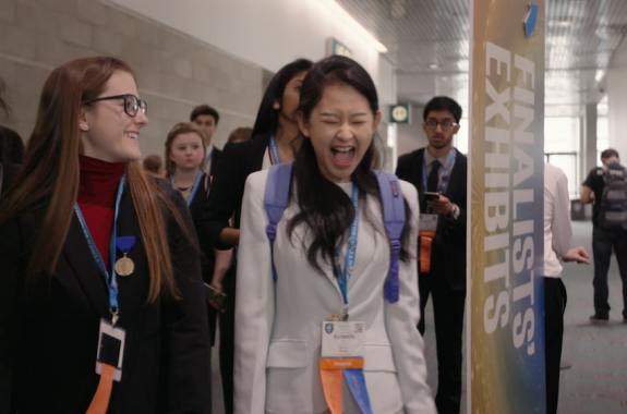 two female students competing at a science fair, they are laughing and smiling
