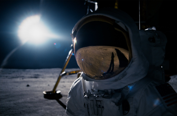 image from film 'first man' of an astronaut on the moon with the lunar module behind him and the reflection of what's in front of him being reflected on his visor