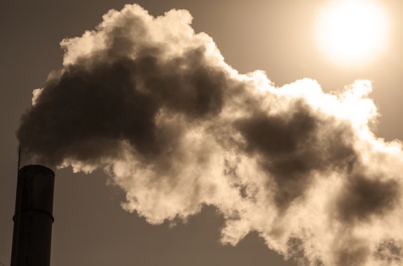 Smoke emanating from a tall chimney stack with the bright sun in the background