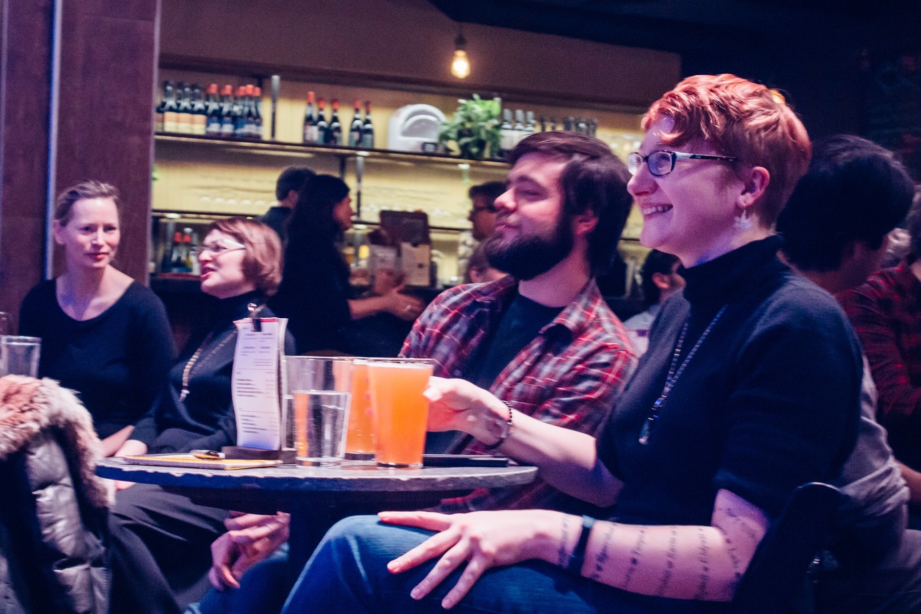 audience members sitting at tables with drinks look on and laugh toward the stage