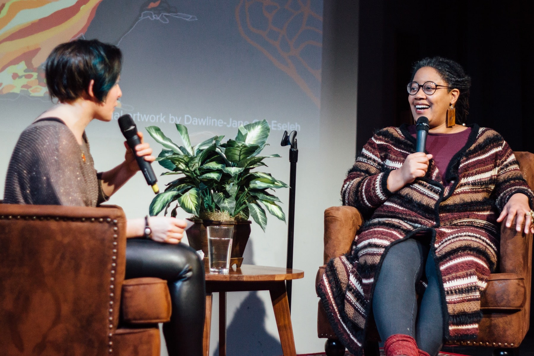 two women sitting onstage with microphones with a plant in between them
