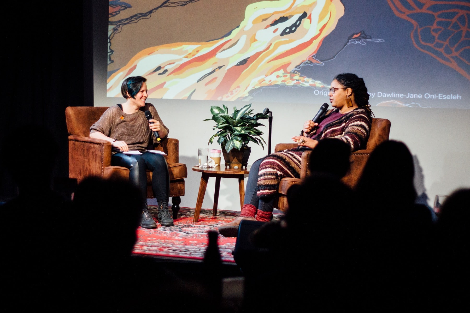 two women sitting onstage with microphones with a plant in between them