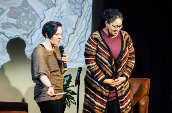 two women, one with a microphone, speaks and the other bows to the crowd