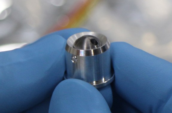 a blue gloved hand holding a silver-colored bullet