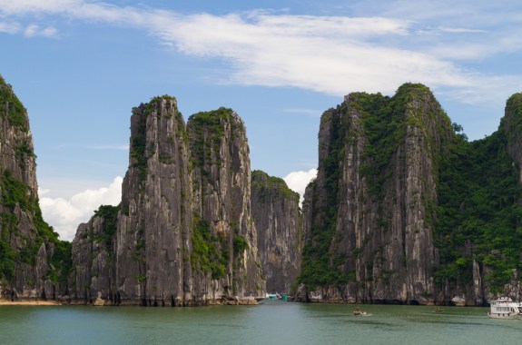 giant rocks topped with green vegetation tower over a beautiful blue bay