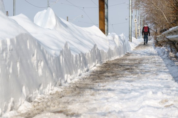 a person walking through the cold, next to a tall wall of snow