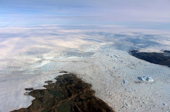the edge of a glacier as seen from the air, which is releasing icebergs into the ocean.