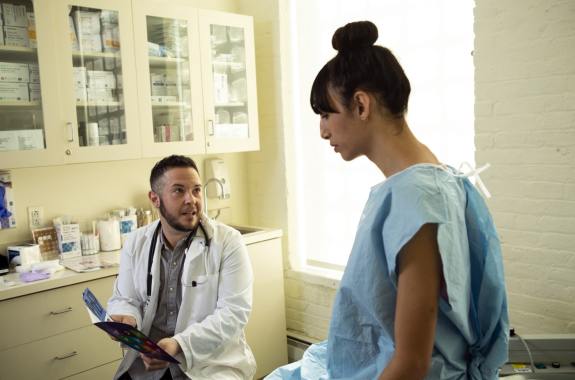 A patient in a hospital gown speaking to her doctor in an exam room.