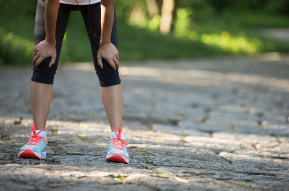 woman bent over on a road wearing running tights and shoes and resting after a workout