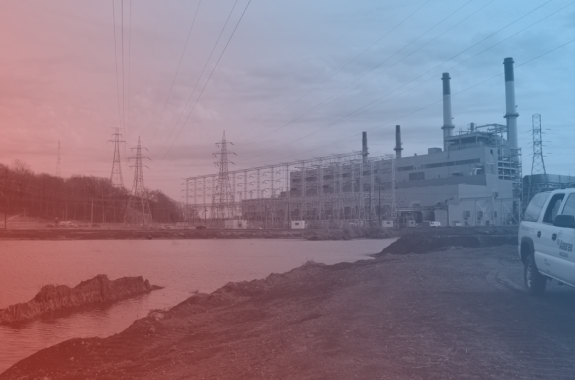 a coal power plant under an overcast sky. next to it in the foreground is a large pool of water that looks more like a lake than a pond with a blue and red filter
