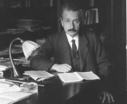mid range black and white photo of einstein in his office working over books and papers