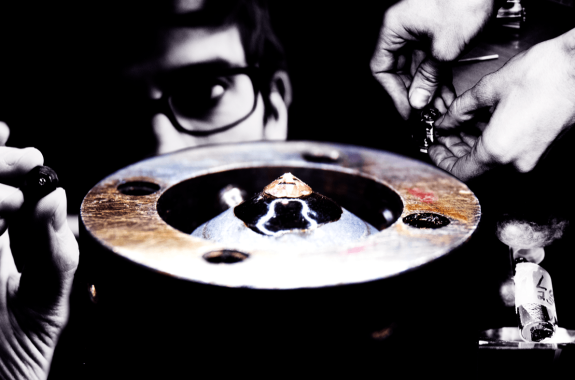 a collage of images including a man holding a small device, a circular looking metal machine part, hands handling a small instrument apart, and a small vial with a label