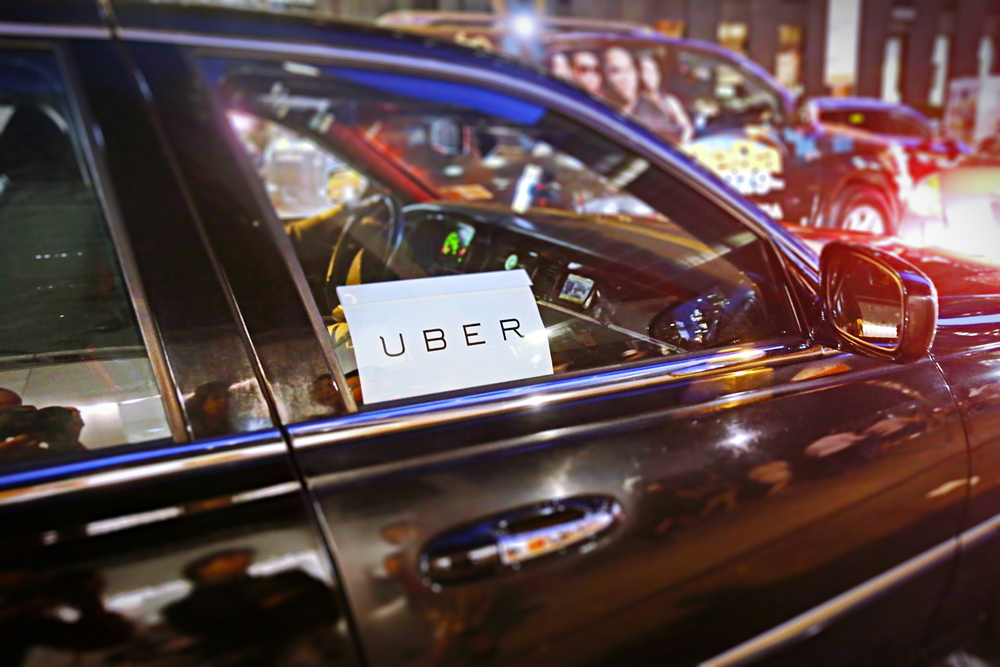 a black car with a sign in the passenger window that reads 'uber' in a busy city street