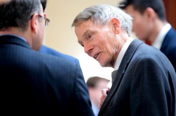 an older white man in a black suit talking to another man in glasses