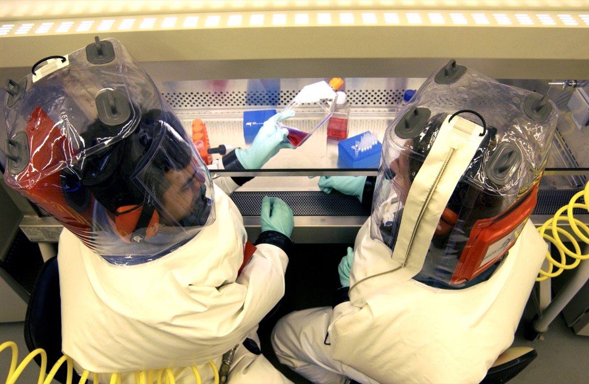 an overhead look at two scientists in puffy safety suits working with some vials