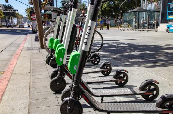 a row of green and black electric scooters with large wheels lined up on a grey sidewalk next to the street
