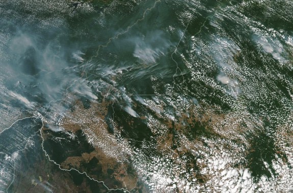 a colored satellite image of a green forest, with large clouds and trails of smoke jetting from it
