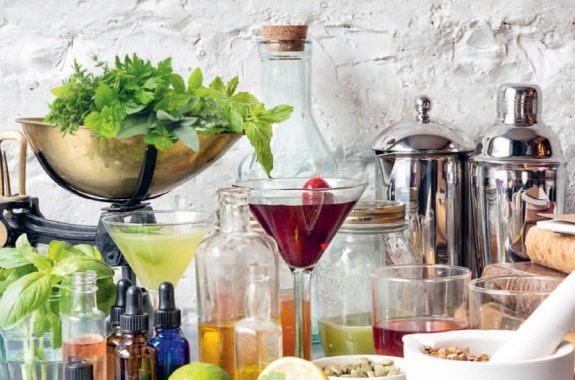 a counter full of cocktails and herbs, bitters, and fruits