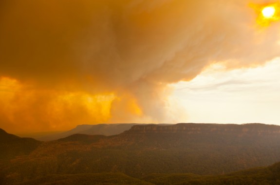 a massive fire in the rolling mountains with a massive smoke plume billowing out