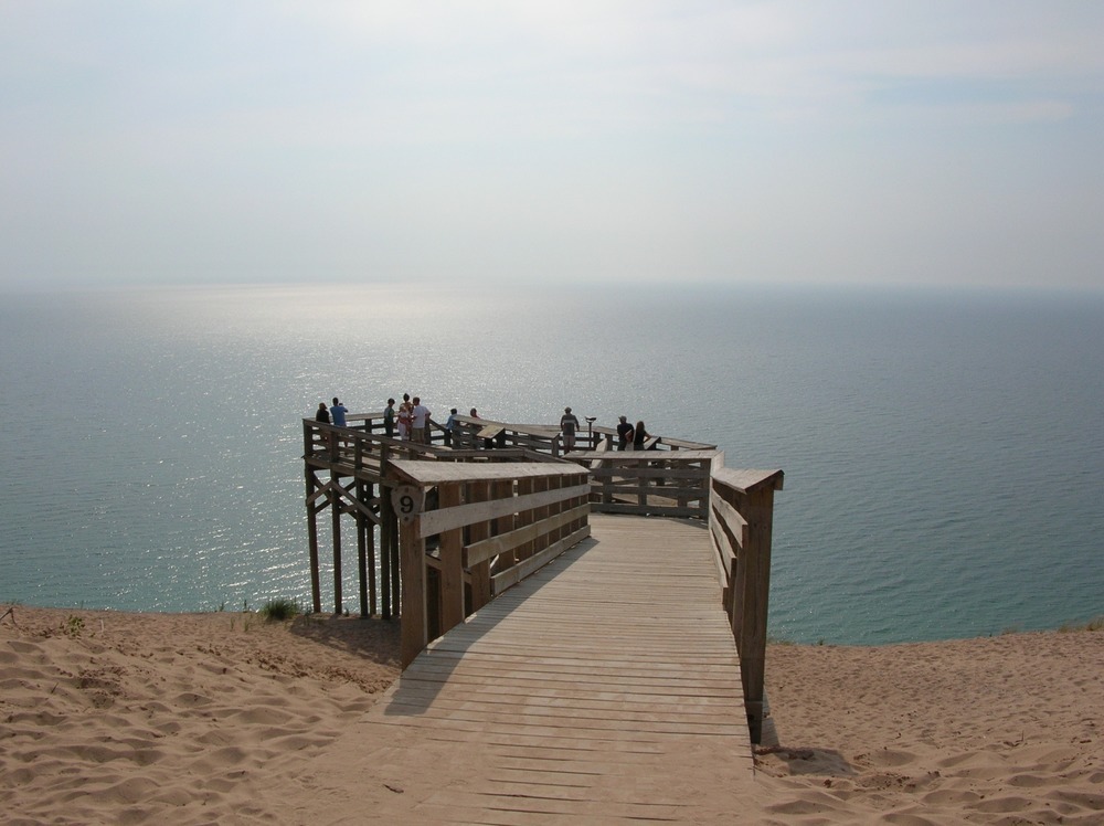 silhouette of multiple people standing on a wooden deck overlooking a grayish blue lake that fades into the background
