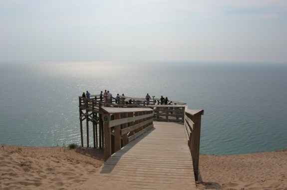 silhouette of multiple people standing on a wooden deck overlooking a grayish blue lake that fades into the background