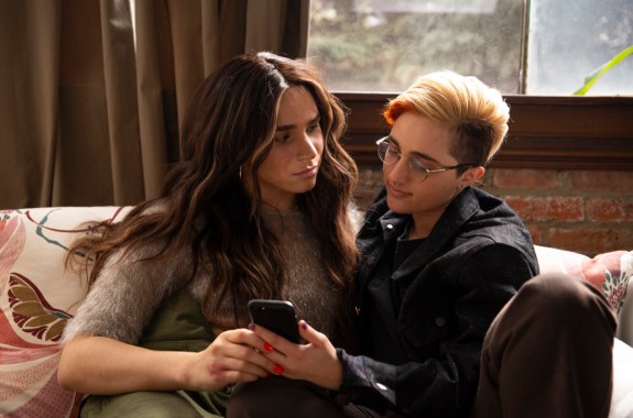 A transfeminine non-binary person and transmasculine gender-nonconforming person looking at a phone with upset expressions