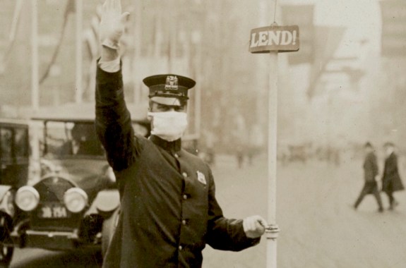 a man in a flat cap, white gloves, and face masks, directs car traffic