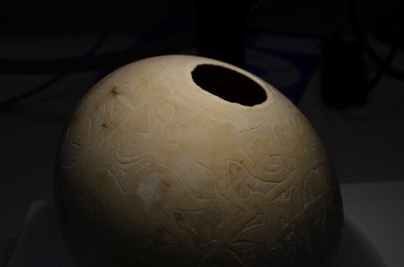 a large egg shell with a hole on the side. there are intricate carvings on its surface