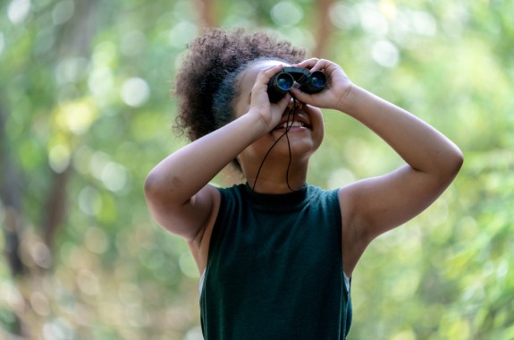 a girl looks through binoculars in nature