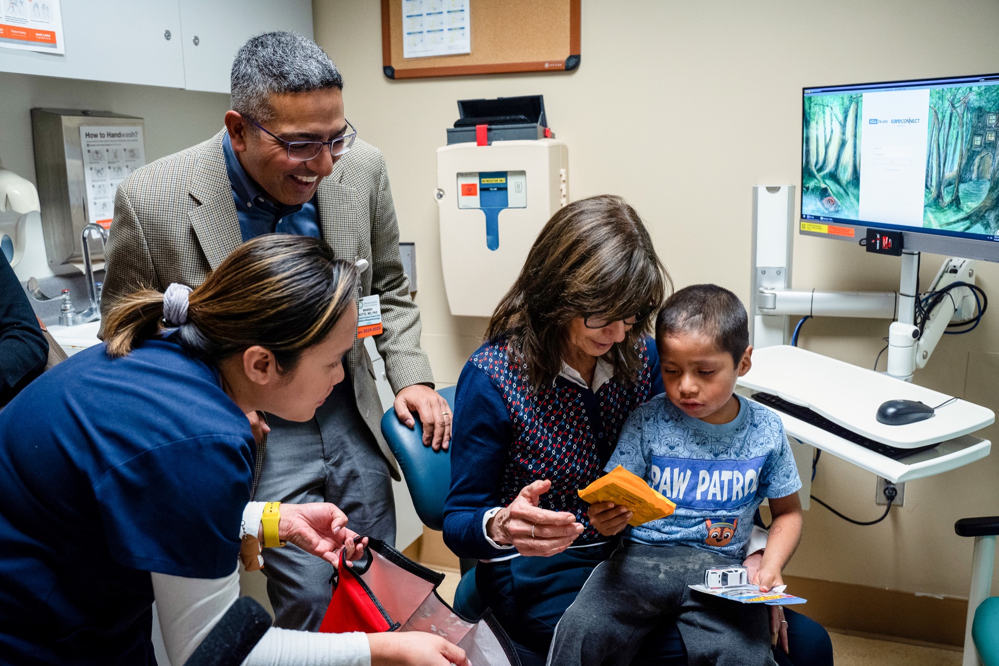 four people in a doctors office. two women -- a nurse and a doctor -- and a man -- also a doctor. a young boy sits in the doctor's office