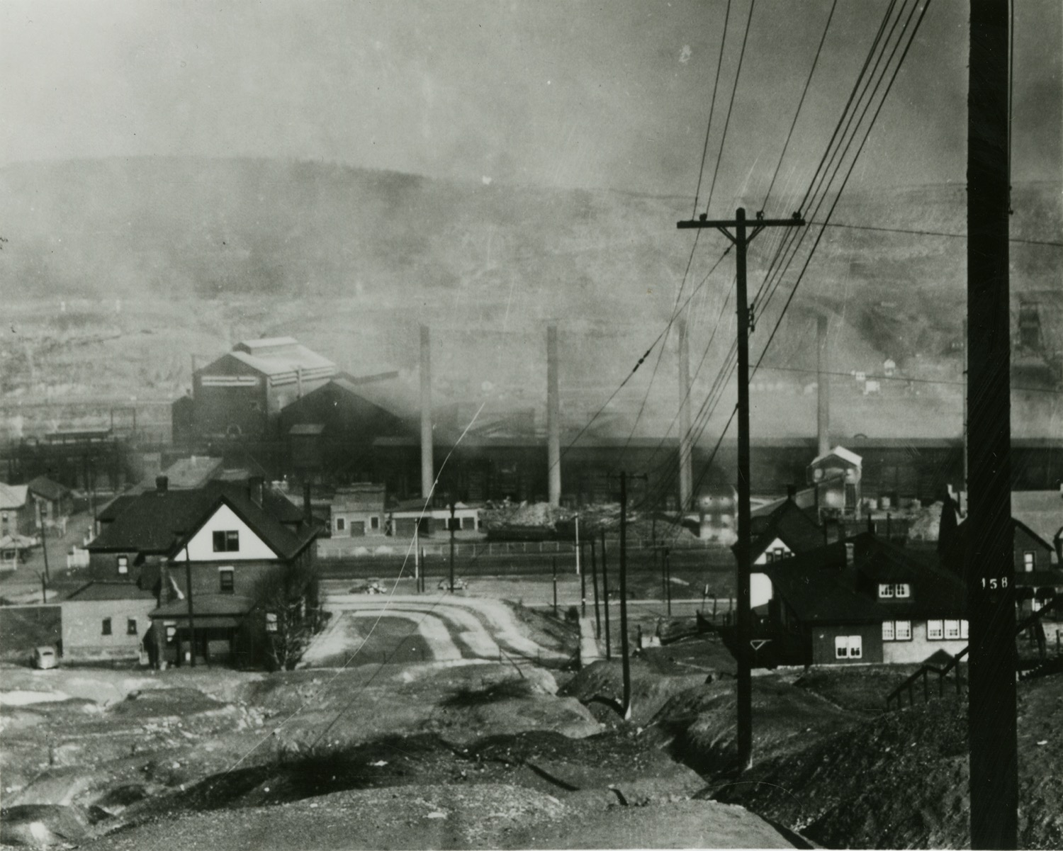 a black and white image of a small town covered in smog. you can see tall smoke stacks