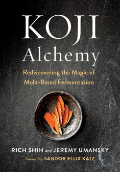 a book cover of vegetables in a gray bowl on a gray table. the title is "koji alchemy" by rich shih and jeremy umansky