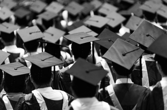 a black and white image of the backs of a group of students in caps and gowns, graduating