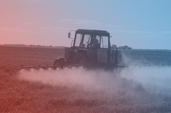 a tractor spraying herbicides and pesticides on a field of crops. the image has a blue and red filter