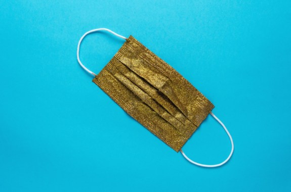 A sparkly gold medical face mask lying flat on a bright blue background