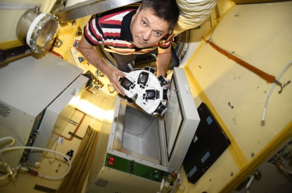 astronaut in striped shirt on space station carrying half circle instrument