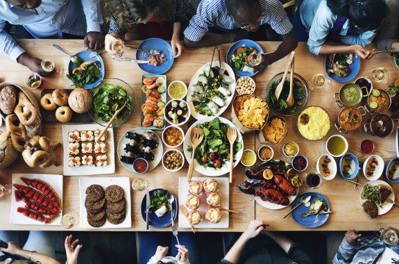 aerial view of a table full of food and drinks with various arms reaching out to eat