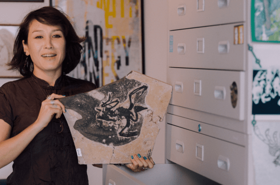 a woman scientist holding a rock with a fossilized bird in an office