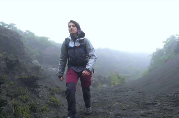 a woman in hiking gear treks through a misty barren volcanic landscape
