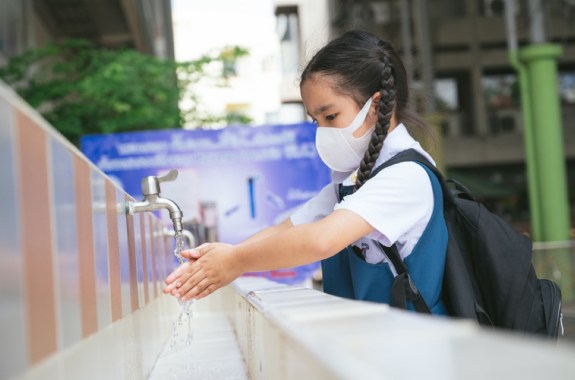 an asian student washing hands at an outdoor wash basin in a school wearing a face mask