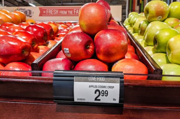 shiny reddish-pink apples stacked in a pyramid in a grocery store with a tag for price of $2.99