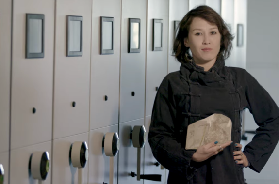 a woman scientist holding a rock with a fossilized bird in a museum collection